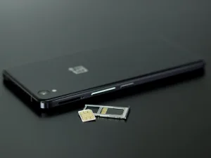 A sleek black smartphone with its SIM card tray ejected, showing a nano-SIM card next to a micro-SIM adapter and a standard SIM card on a dark surface.