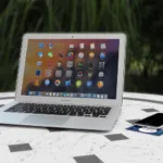 Open laptop with colorful app icons on screen placed on a white round table beside a smartphone.