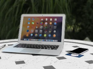 Open laptop with colorful app icons on screen placed on a white round table beside a smartphone.