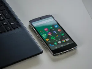 Smartphone with colorful app icons on screen lying next to a laptop on a white surface.