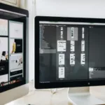 Two computer monitors on a desk displaying a website design project and a folder structure in a professional workspace.