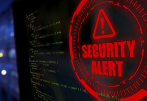 Computer screen displaying code with a prominent red 'SECURITY ALERT' warning symbol in the foreground, indicating a cybersecurity threat.