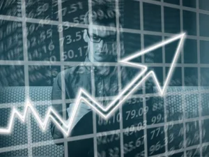 Double exposure of a focused person analyzing financial data with a rising arrow graph overlay indicating stock market growth.